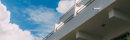 panoramic shot of modern building against blue sky with white cloudsの写真素材