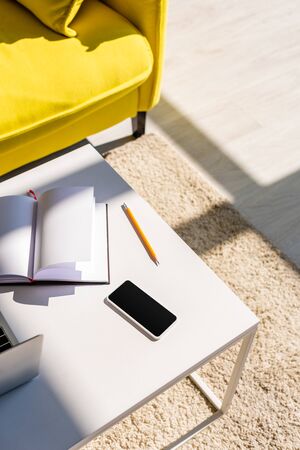 living room with sofa and table with laptop, smartphone and notepad in sunlightの写真素材