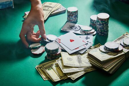 partial view of female hand with casino tokens, playing cards and money on green backgroundの写真素材