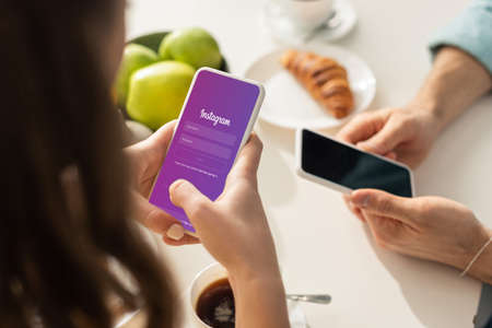 KYIV, UKRAINE - FEBRUARY 21, 2020: Selective focus of woman using smartphone with instagram app near boyfriend during breakfast in kitchenのeditorial素材
