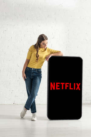 KYIV, UKRAINE - FEBRUARY 21, 2020: Attractive young woman standing near model of smartphone with netflix appのeditorial素材