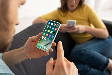 KYIV, UKRAINE - FEBRUARY 21, 2020: Selective focus of man holding smartphone with iphone screen near woman on couchのeditorial素材