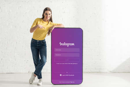KYIV, UKRAINE - FEBRUARY 21, 2020: Smiling woman pointing with finger at model of smartphone with instagram appのeditorial素材