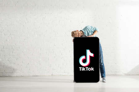 KYIV, UKRAINE - FEBRUARY 21, 2020: Positive man with closed eyes hugging huge model of smartphone with tik tok appのeditorial素材