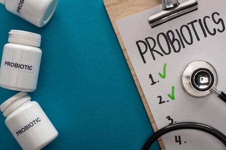 top view of clipboard with probiotics empty list with stethoscope near containers with pills on blue backgroundの写真素材
