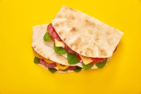 fresh sandwiches with salami, pita, vegetables and cheese on yellow backgroundの写真素材