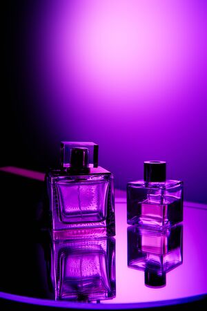 Violet perfume bottles on round mirror surface and light spot on backgroundの写真素材