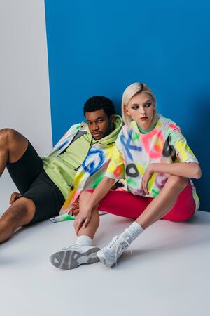 multicultural couple posing in colorful futuristic look on grey and blue