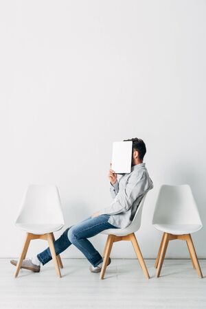 Side view of employee covering face with laptop while sitting on chairの写真素材