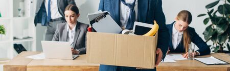 Panoramic shot of dismissed man holding box with papers and digital tablet in office