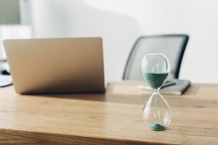 Selective focus of hourglass on table near laptop in office