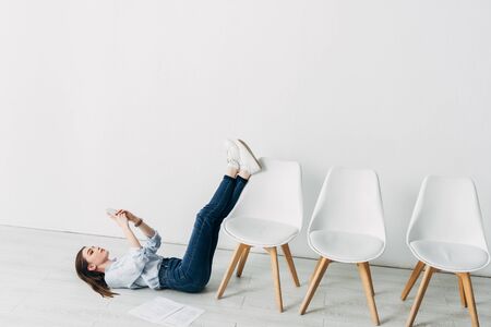 Side view of attractive employee using smartphone near resume on floorの写真素材