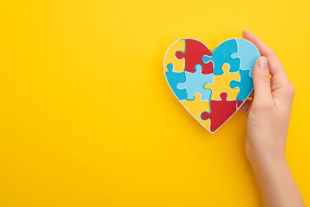 cropped view of woman holding puzzle heart on yellowの写真素材