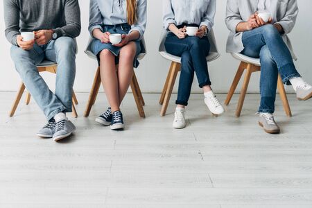 Cropped view of colleagues holding coffee cups on chairs in officeの写真素材