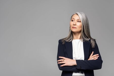 confident asian stylish businesswoman with grey hair and crossed arms isolated on greyの写真素材