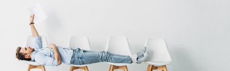 Panoramic shot of employee holding resume while lying on chairs in officeの写真素材
