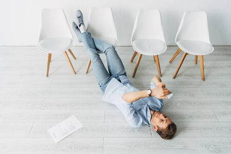 High angle view of employee using smartphone near resume on floor