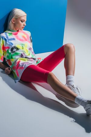 beautiful fashionable girl posing in neon pink bike shorts and colorful t-shirt on grey and blue
