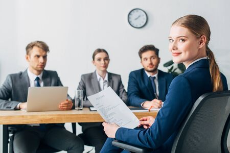 Selective focus of employee looking at camera while holding resume near recruitersの写真素材