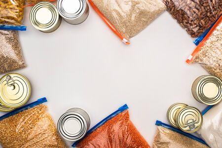 top view of cans and groats in zipper bags on white background, food donation conceptの写真素材