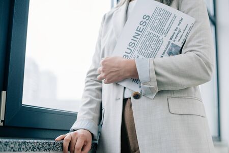cropped view of professional businesswoman holding business newspaper in office