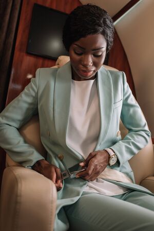 attractive african american businesswoman fastening safety belt in private jetの写真素材