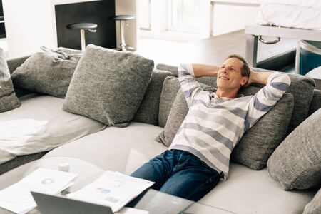 cheerful man relaxing on sofa near charts and graphs on coffee tableの写真素材
