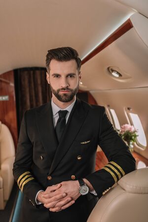 handsome, confident pilot looking at camera while standing in plane