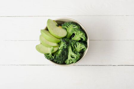 top view of fresh green apple and broccoli on white wooden surfaceの写真素材