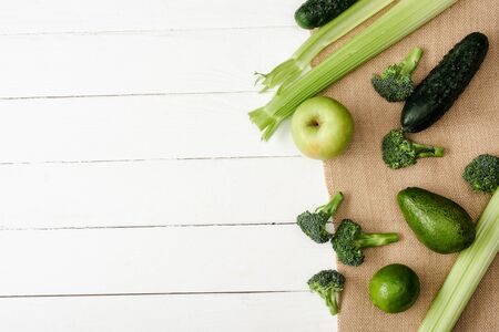 top view of fresh green fruits and vegetables on sackcloth on white wooden surface