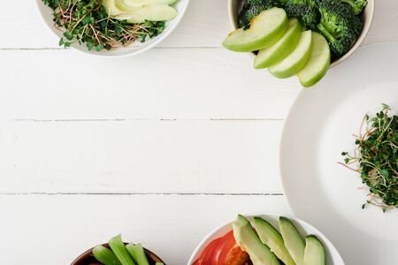 top view of fresh vegetables and fruits with microgreen in bowls on white wooden surfaceの写真素材