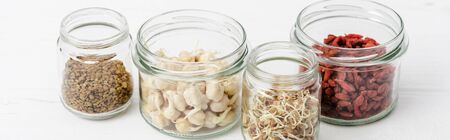 goji berries and sprouts in glass jars on white wooden surface, panoramic orientationの写真素材