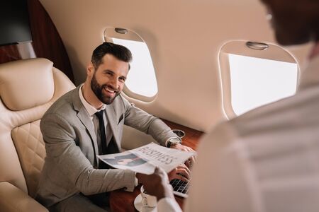 selective focus of handsome businessman looking at african american stewardess giving him newspaperの写真素材