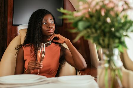 selective focus of dreamy african american woman holding glass of champagne in private jet