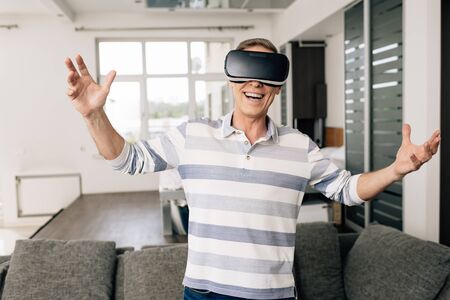 happy man in virtual reality headset with outstretched hands at homeの写真素材