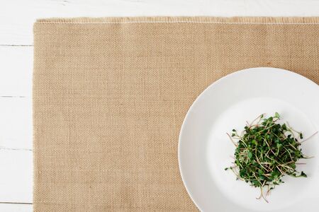top view of fresh microgreen on plate on beige napkin on white wooden surfaceの写真素材