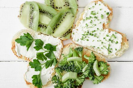 top view of heart shaped canape with creamy cheese, broccoli, microgreen, parsley and kiwi on white wooden surfaceの写真素材