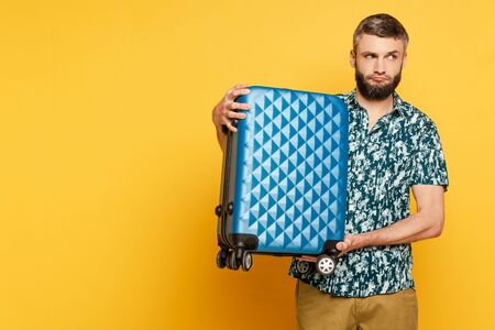 sad bearded guy with blue suitcase on yellowの写真素材