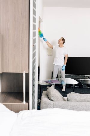 selective focus of cheerful man holding duster brush while cleaning living roomの写真素材