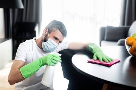 Man in medical mask cleaning table in living roomの写真素材
