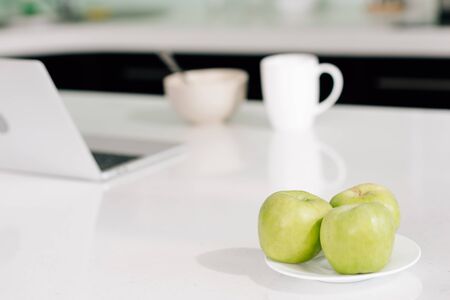 selective focus of green apples near laptop, bowl and cup on tableの写真素材