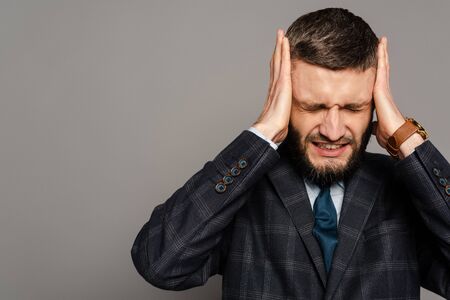 handsome bearded businessman in suit covering ears with hands on grey backgroundの写真素材