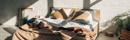 bedroom interior with bed, pillows and paintings in sunlight with shadows, panoramic orientation