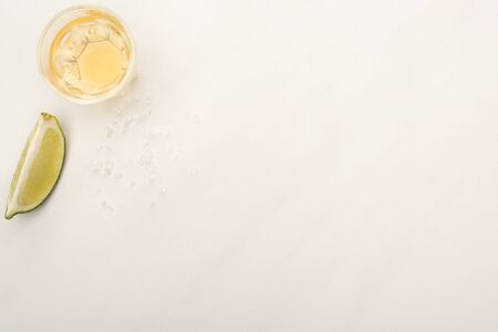 top view of golden tequila with lime on white marble surface