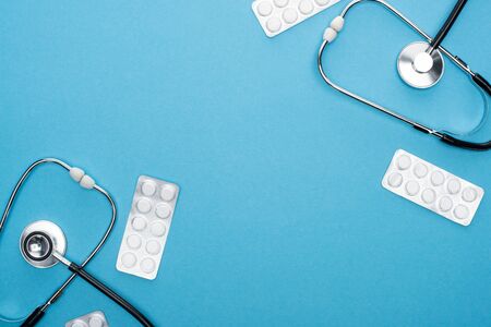 top view of pills in blister packs and stethoscopes on blue backgroundの写真素材