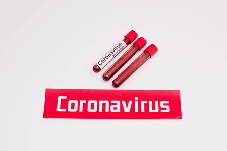 High angle view of card with coronavirus lettering near test tubes with blood samples on whiteの写真素材