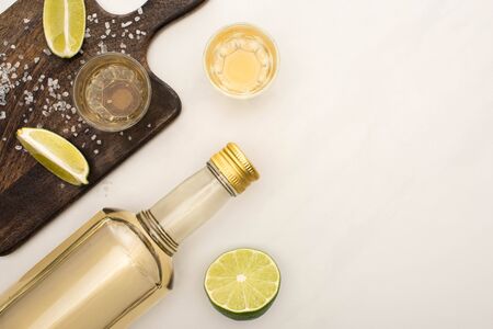 top view of golden tequila with lime, salt on wooden cutting board on white marble surfaceの写真素材
