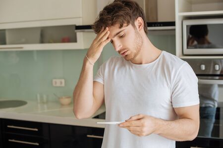 worried ill man looking at thermometer at home on self isolationの写真素材