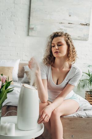 attractive girl sitting in bedroom with air purifier and tulip flowersの写真素材