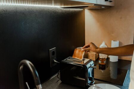 Cropped view of african american woman taking out toast from toaster in kitchenの写真素材